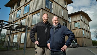 Claus Gyldendahl Christensen (tv.) og Erik Nedergaard Jensen er to generationer af medarbejdere og tillidsmænd i Hustømrerne. I baggrunden ses et stort etagebyggeri i træ, som Hustømrerne har opført i Trige uden for Aarhus.