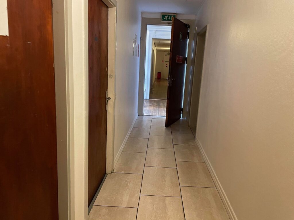 Skoene klistrer til det fedtede gulv, når man går op ad gangene hos Rooms DK. På de små værelser er der tidligere blevet begået drab og voldsomme overfald.
