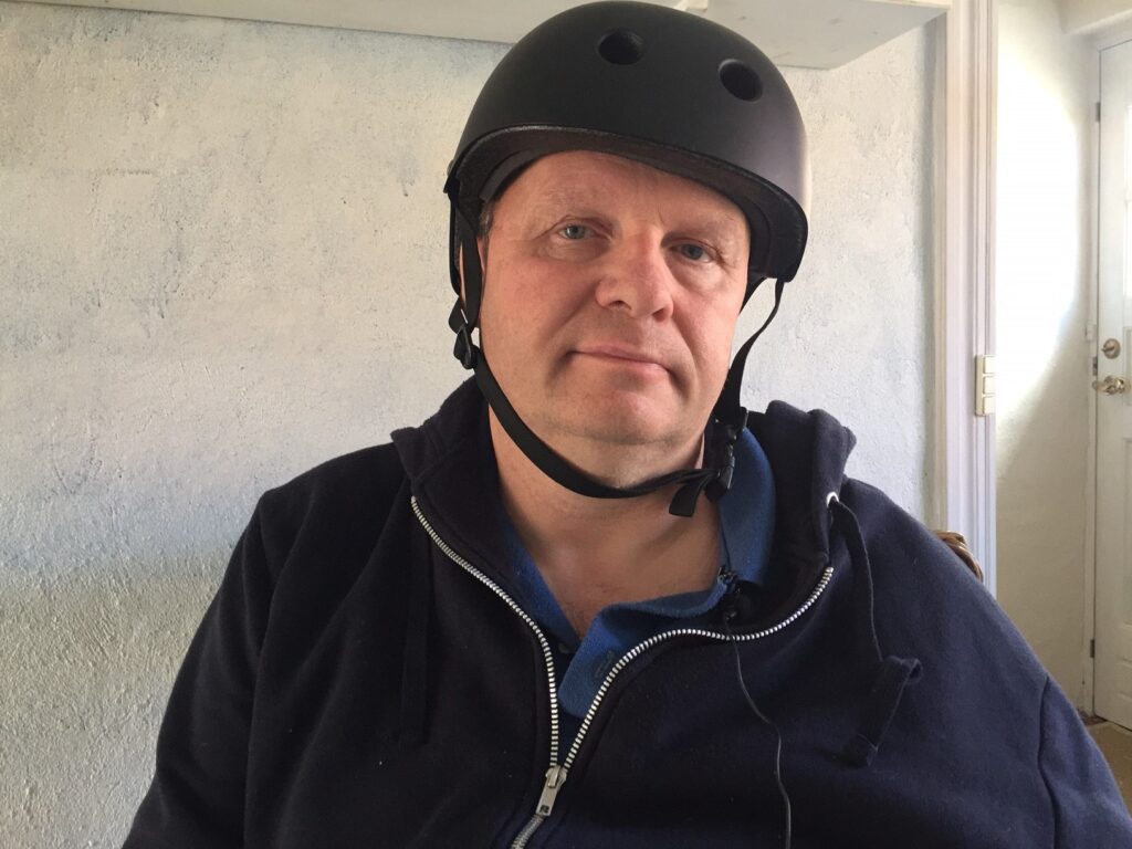 Erik Schack beskytter sin ubeskyttede halvdel af hjernen med en hjelm, da et enkelt stød kan slå ham ihjel. 