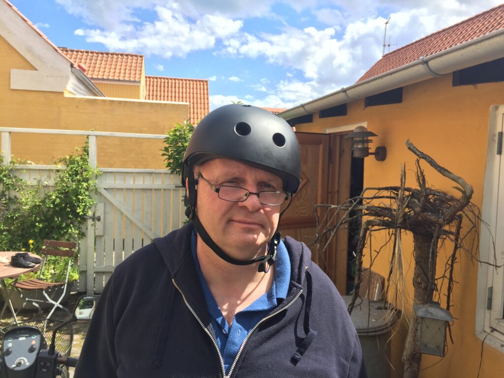 Erik Schack beskytter sin ubeskyttede halvdel af hjernen med en hjelm, da et enkelt stød kan slå ham ihjel. 